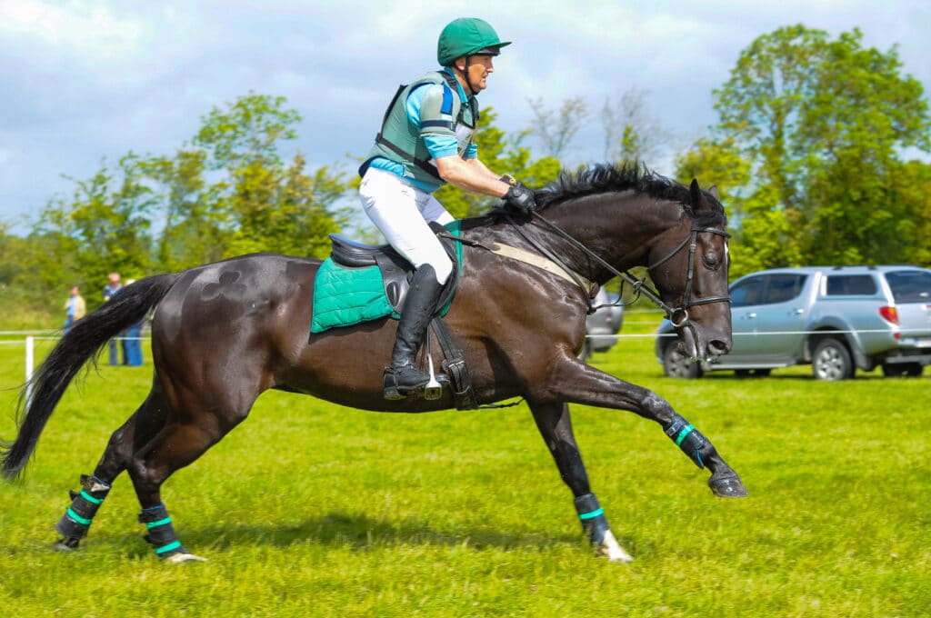 A side view of a rider riding a horse in a horse stable